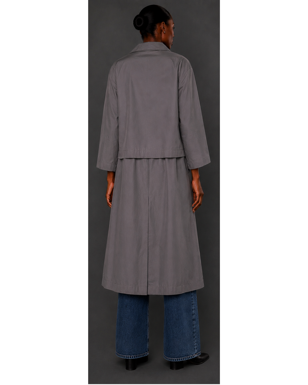 Person wearing a gray coat and blue jeans on a plain background