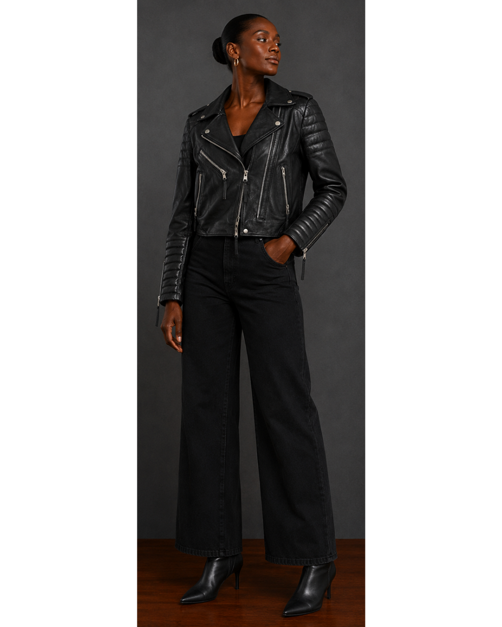 Person wearing a black leather jacket and pants against a gray background