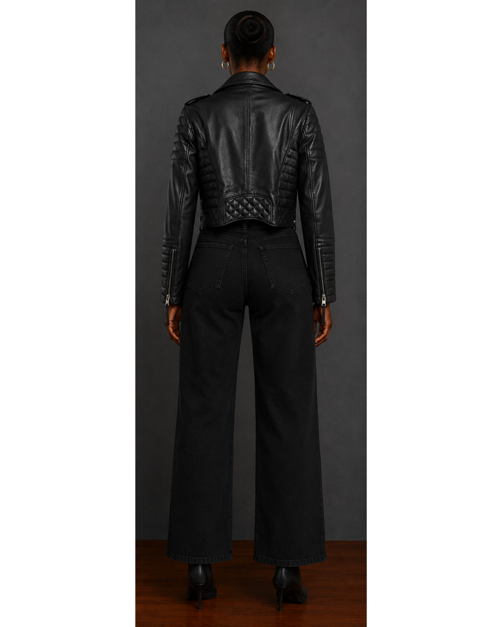 Person wearing a black leather jacket and pants against a gray background