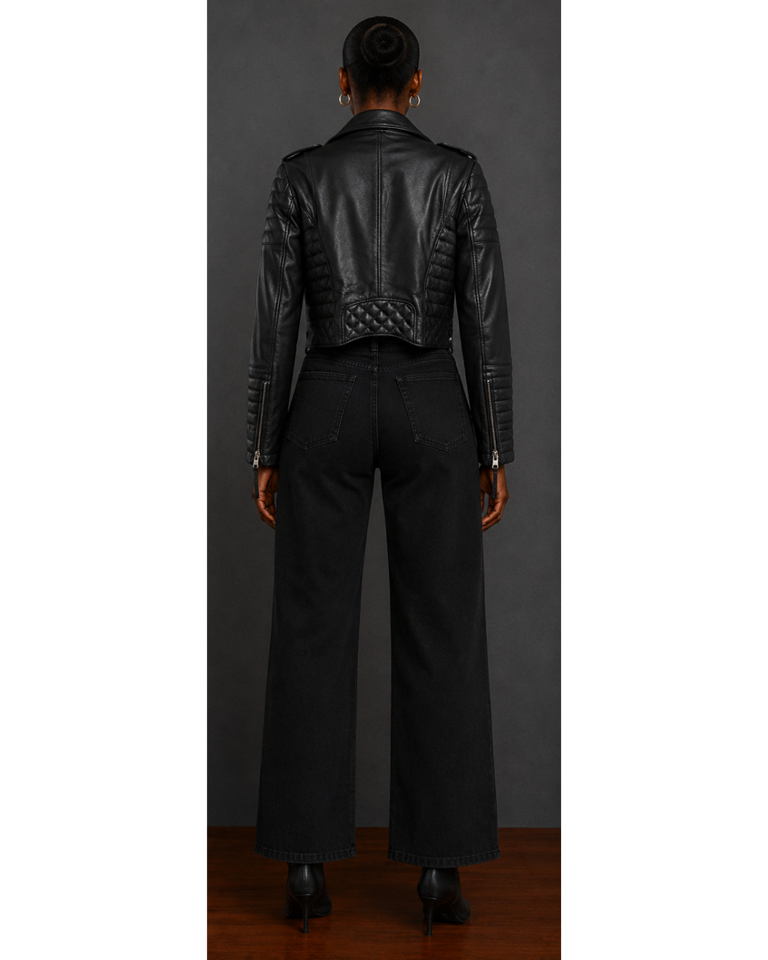 Person wearing a black leather jacket and pants against a gray background