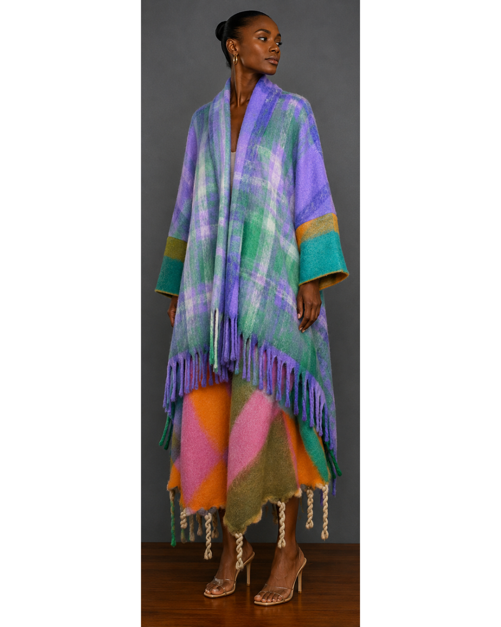 Front view of woman wearing a colorful plaid poncho with fringe details on a gray background