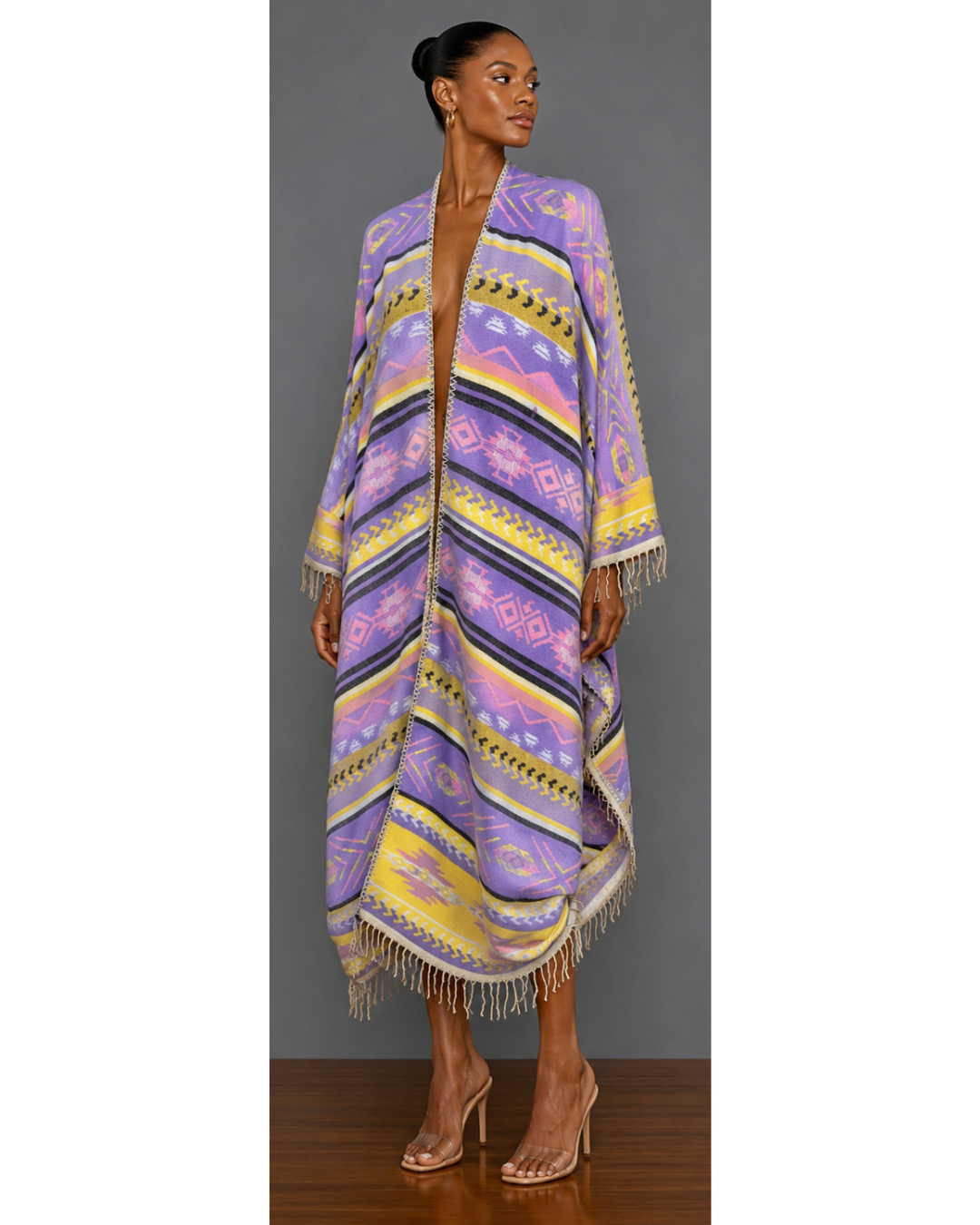 Front view of a woman wearing a colorful patterned blanket wrap coat with fringe against a gray background
