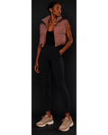 Person wearing a brown puffer vest, black leggings, and beige sneakers on a black background