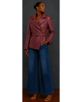 Woman wearing a burgundy leather jacket and blue jeans against a gray background