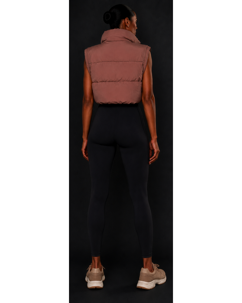 Person wearing a brown puffer vest and black leggings on a black background