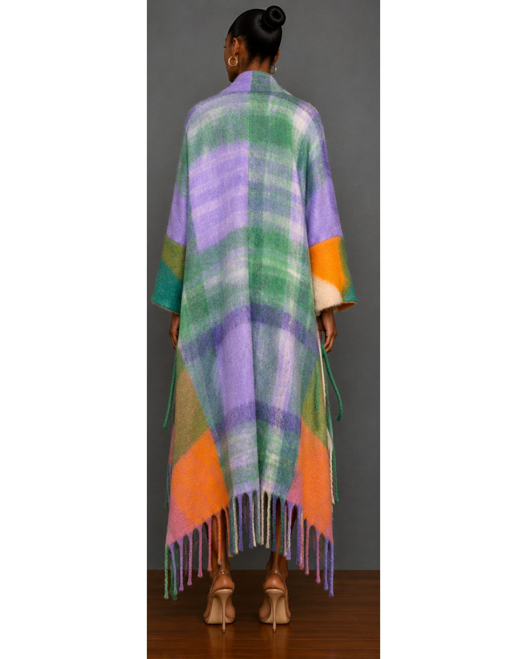 Back view of woman wearing a colorful plaid poncho with fringe details on a gray background