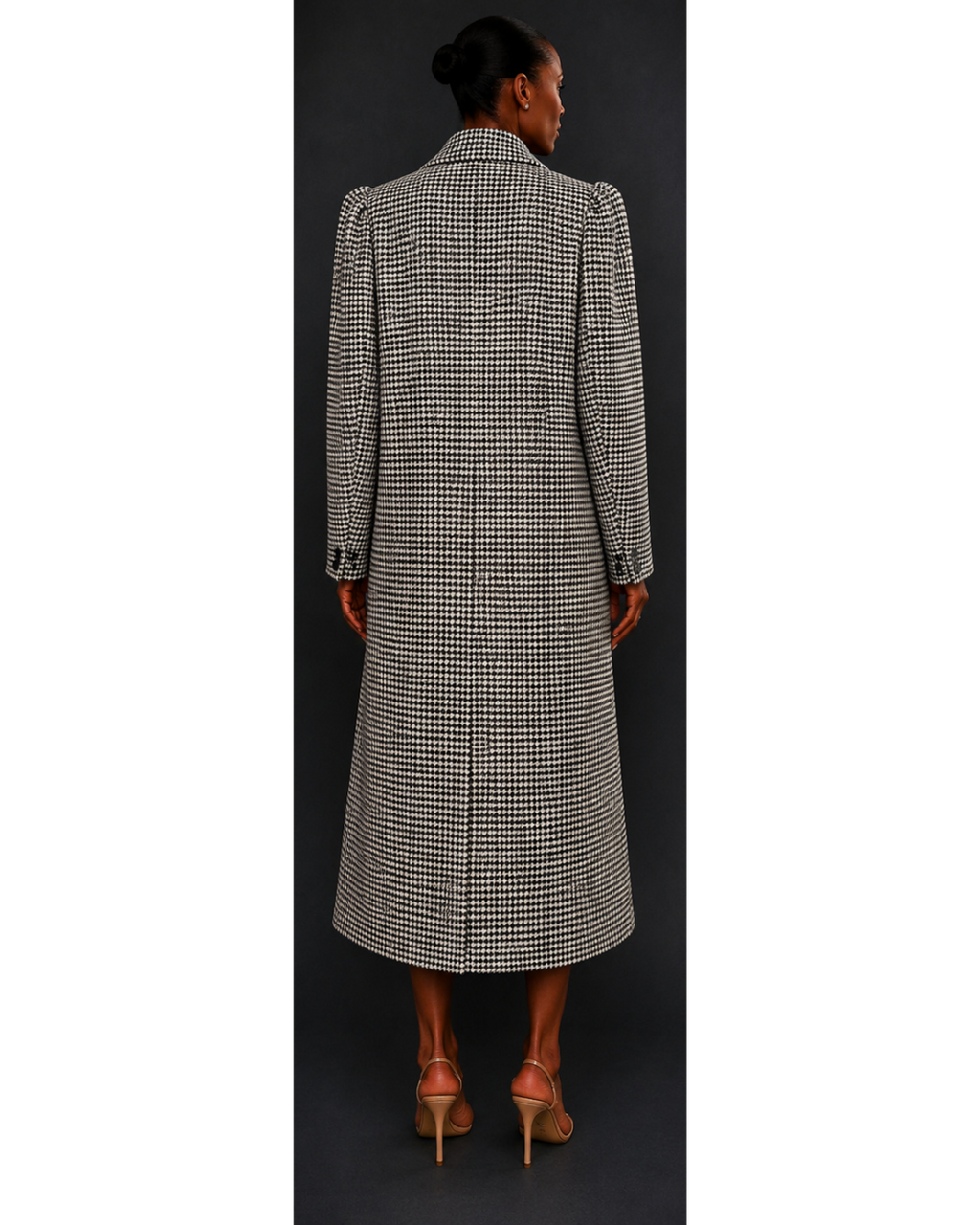 Woman wearing a long, houndstooth coat against a dark background