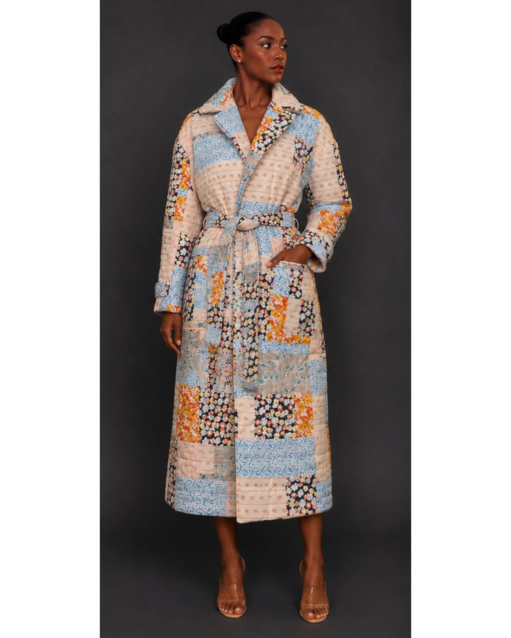 Front view of a woman wearing a long, patterned quilted blanket coat against a dark background