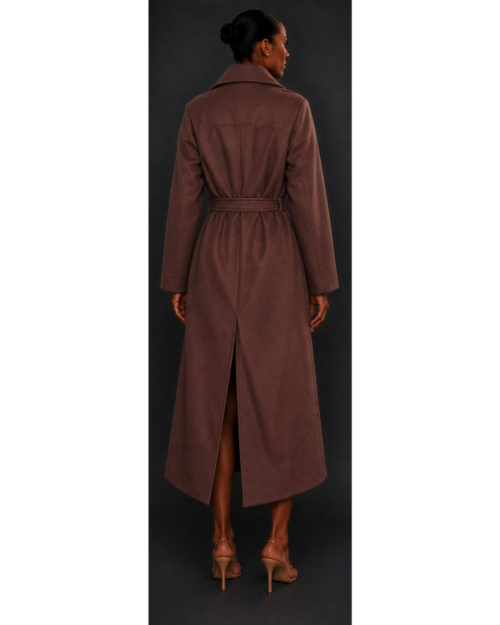 Woman wearing a long brown coat with a belt, standing against a dark background.