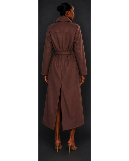 Woman wearing a long brown coat with a belt, standing against a dark background.