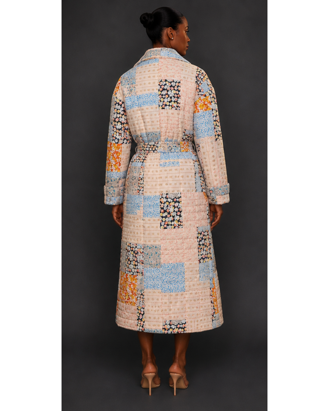 Back view of a woman wearing a long, patterned quilted blanket coat against a dark background