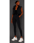 Woman wearing a black sleeveless jacket, black leggings, and white sneakers on a gray background