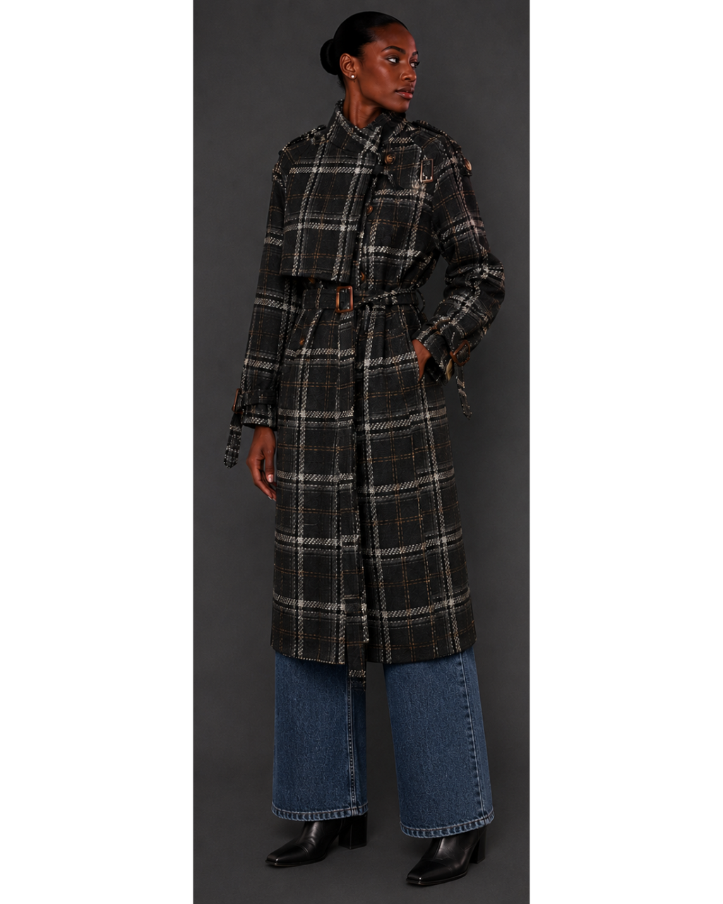 Person wearing a long plaid coat with a belt, standing against a gray background