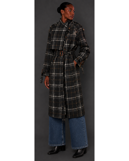 Person wearing a long plaid coat with a belt, standing against a gray background